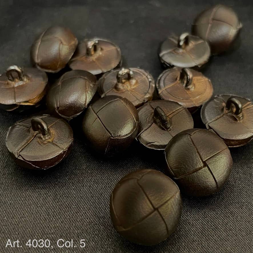 Close-up of Buttonology Inc leather shank buttons with stitched design on dark fabric background