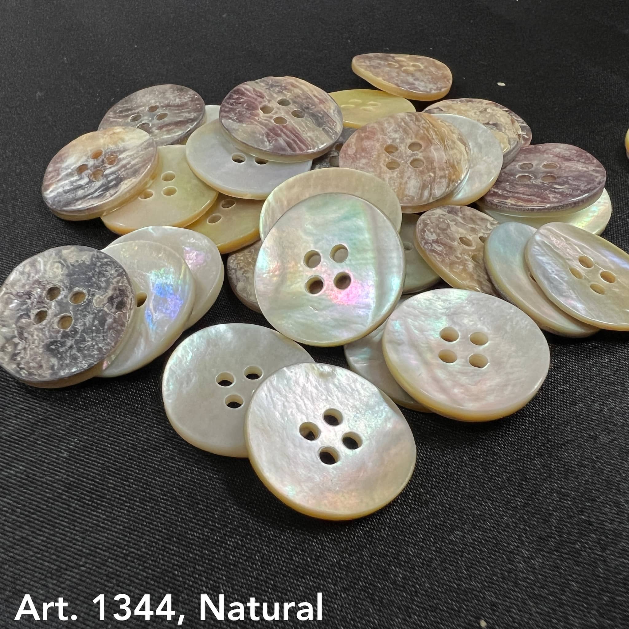 Natural Akoya buttons by Buttonology Inc displayed on black fabric with pearlescent and earthy tones