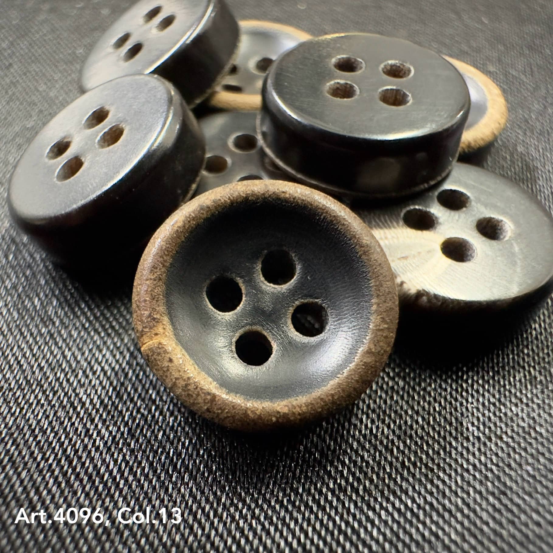 Black and brown natural Real horn buttons with four holes laid on dark fabric by Buttonology Inc