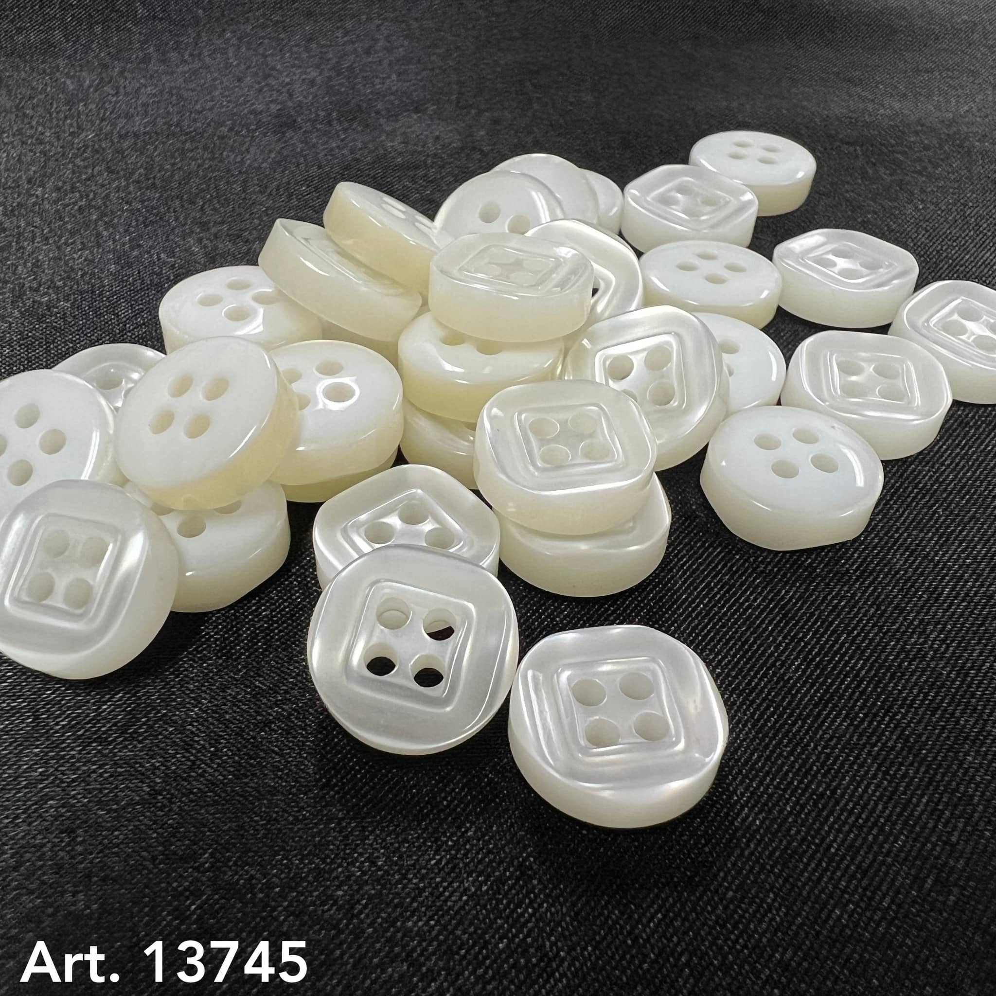 Four-hole sewing buttons by Buttonology Inc in white pearl finish on black fabric background