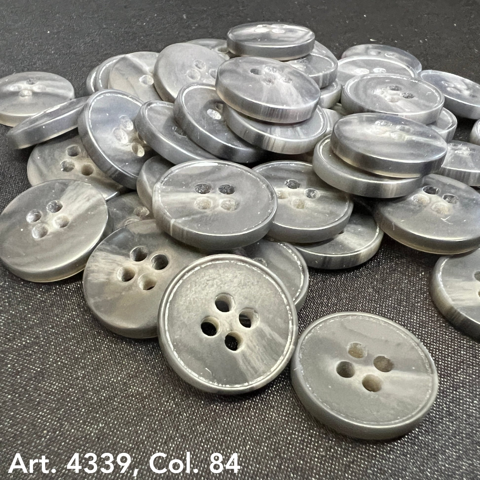 Gray plastic buttons sewing buttons with four holes by Buttonology Inc scattered on dark fabric
