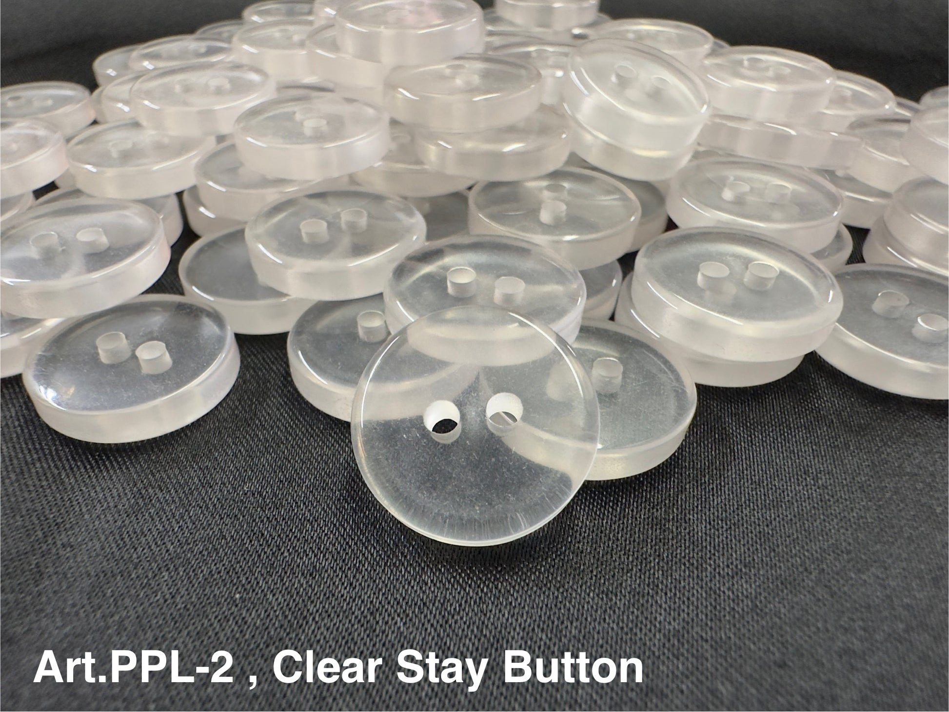 Buttonology Inc clear stay button 2-hole translucent round sewing buttons piled on black fabric