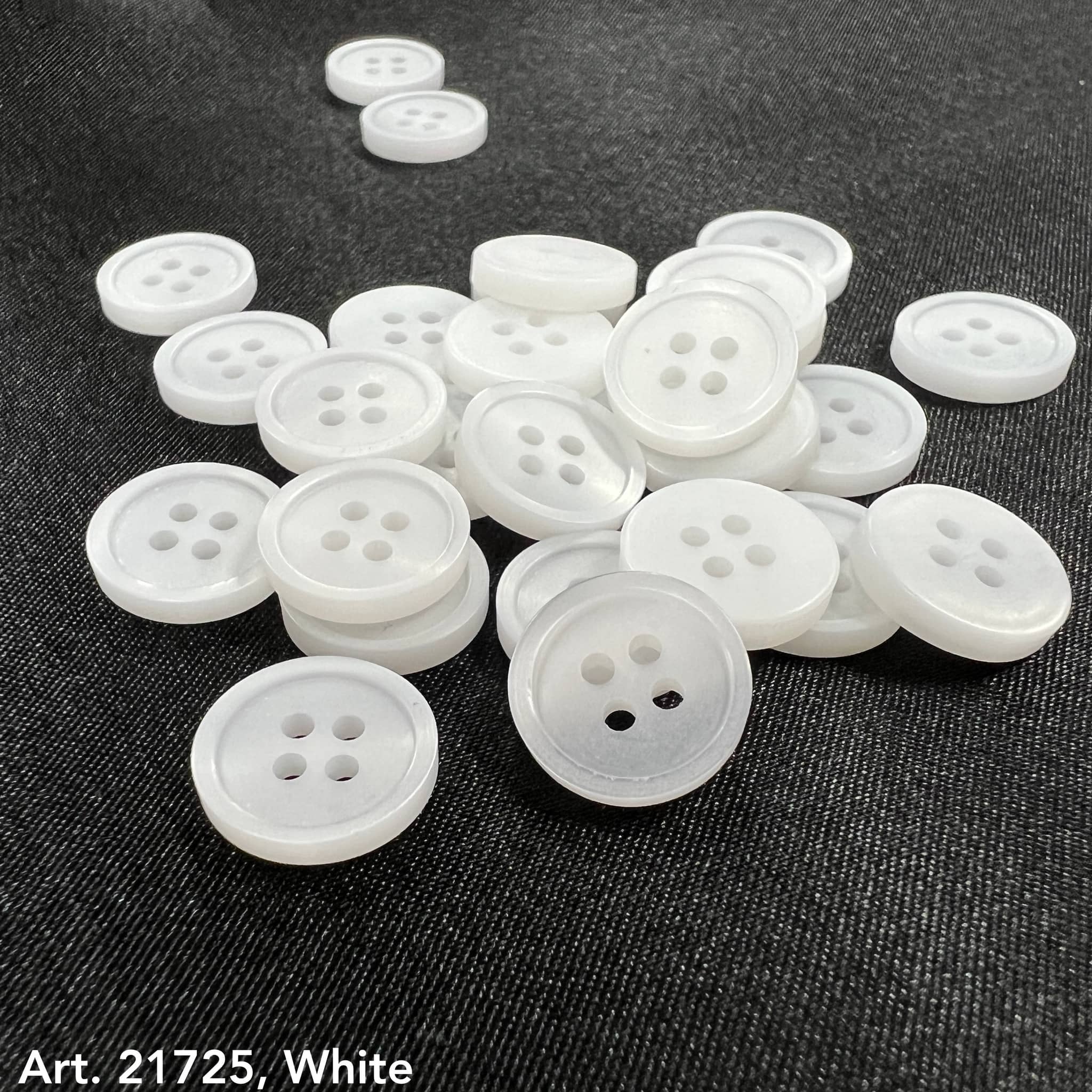 White buttons from the premium button collection by Buttonology Inc spread on dark fabric background