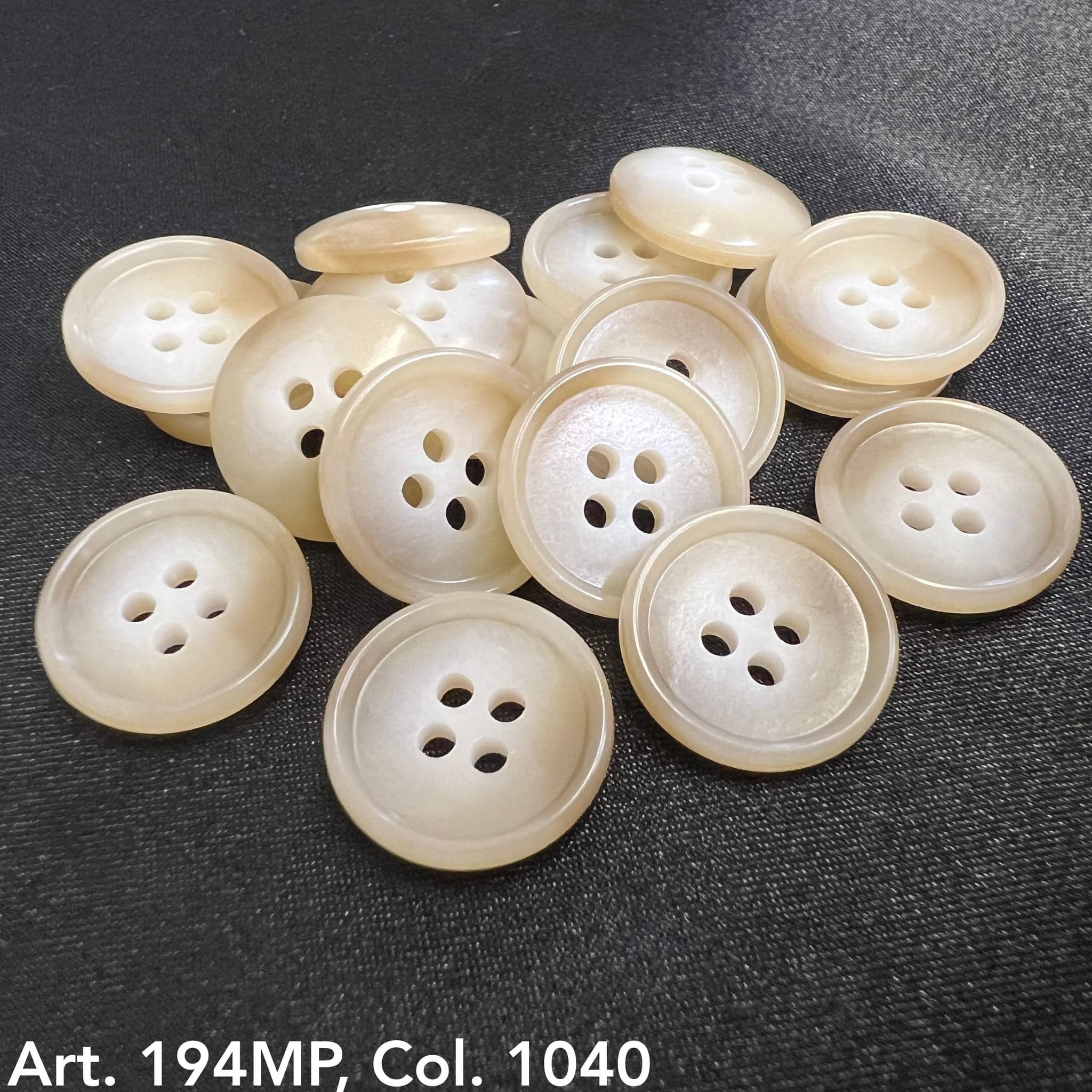 Premium suit buttons by Buttonology Inc in a glossy beige finish with four holes on black fabric