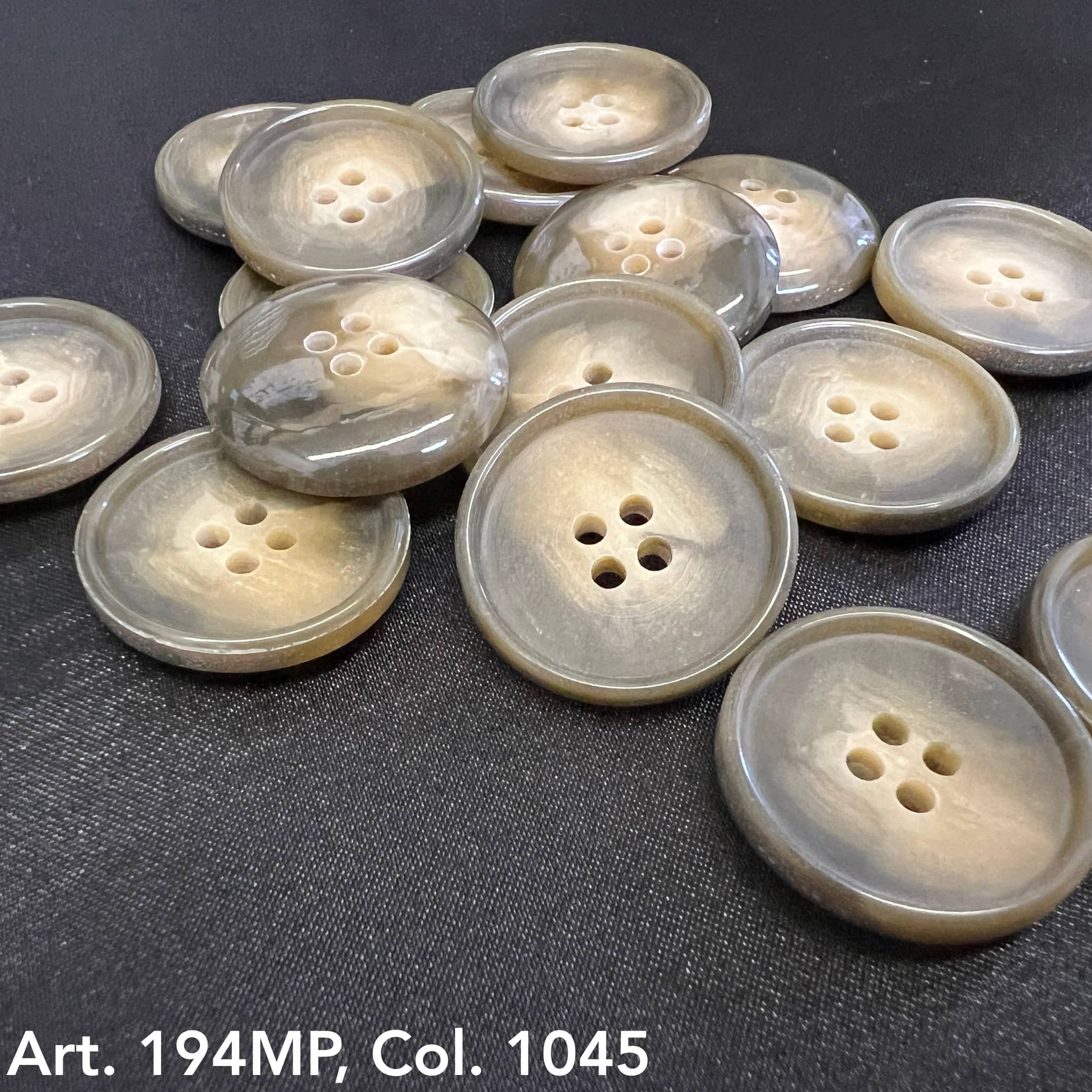 Premium suit buttons by Buttonology Inc in glossy beige and gray tones with four holes on black fabric background