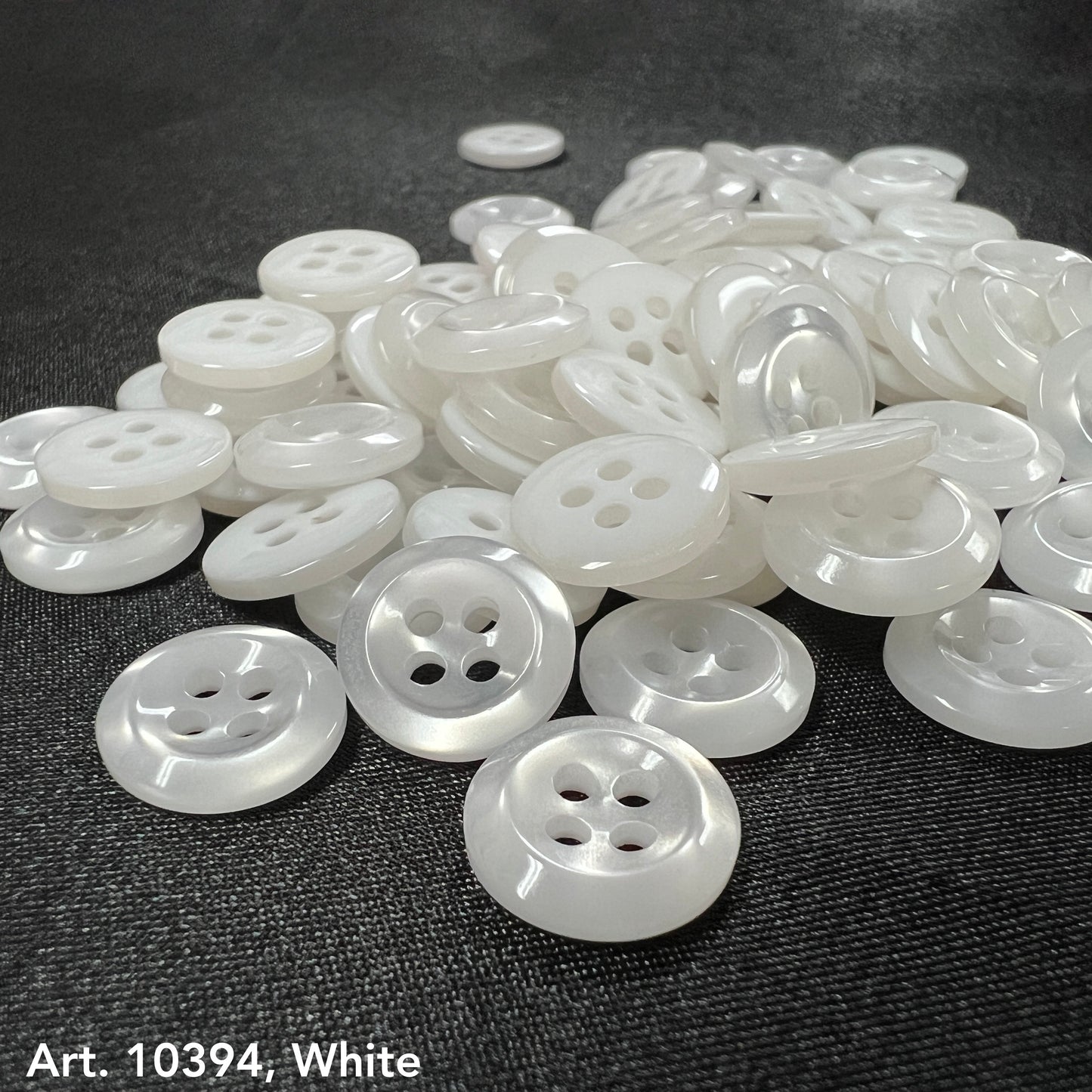 Premium white buttons for crafts by Buttonology Inc scattered on a dark fabric background