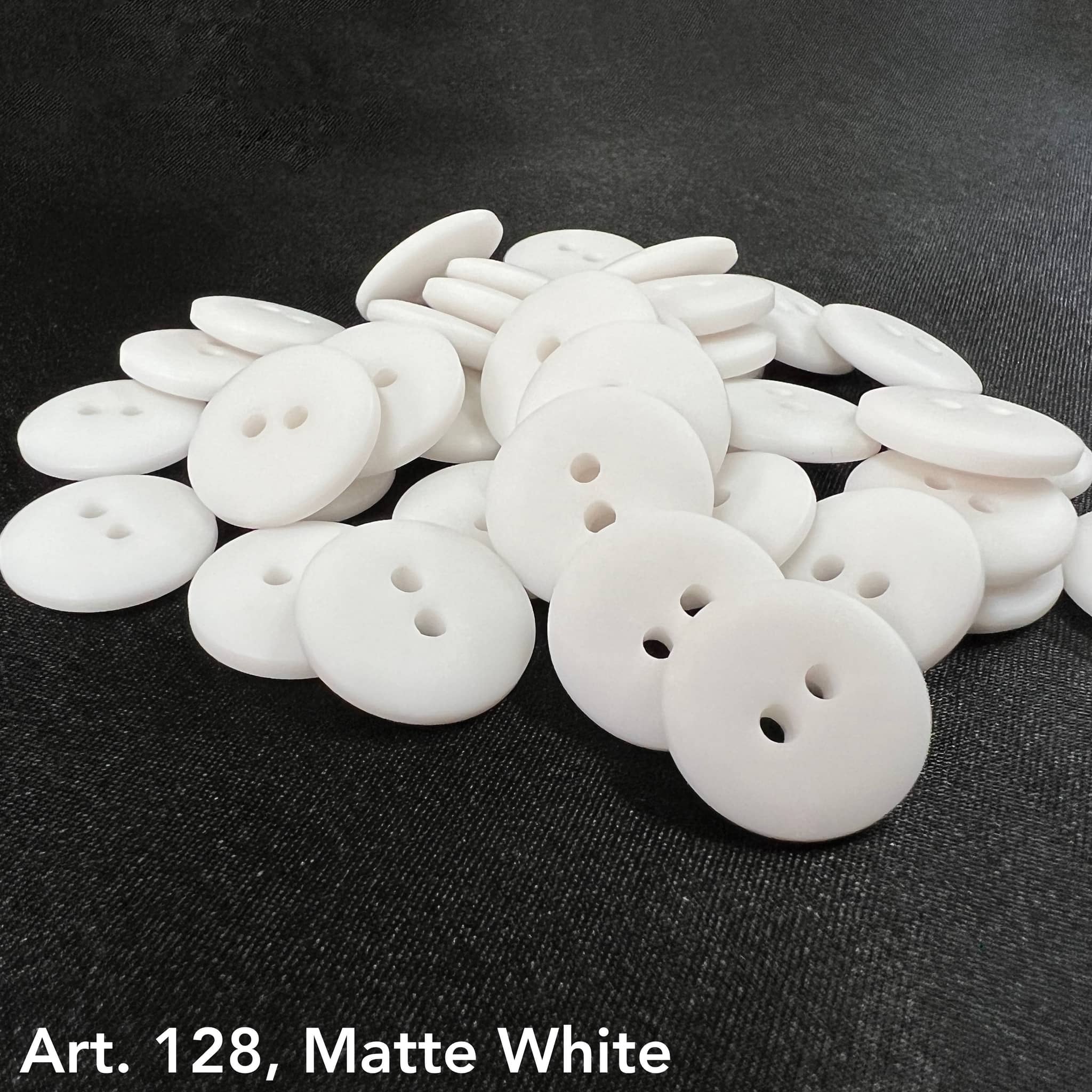 Pile of premium white buttons with a matte finish by Buttonology Inc on black fabric background