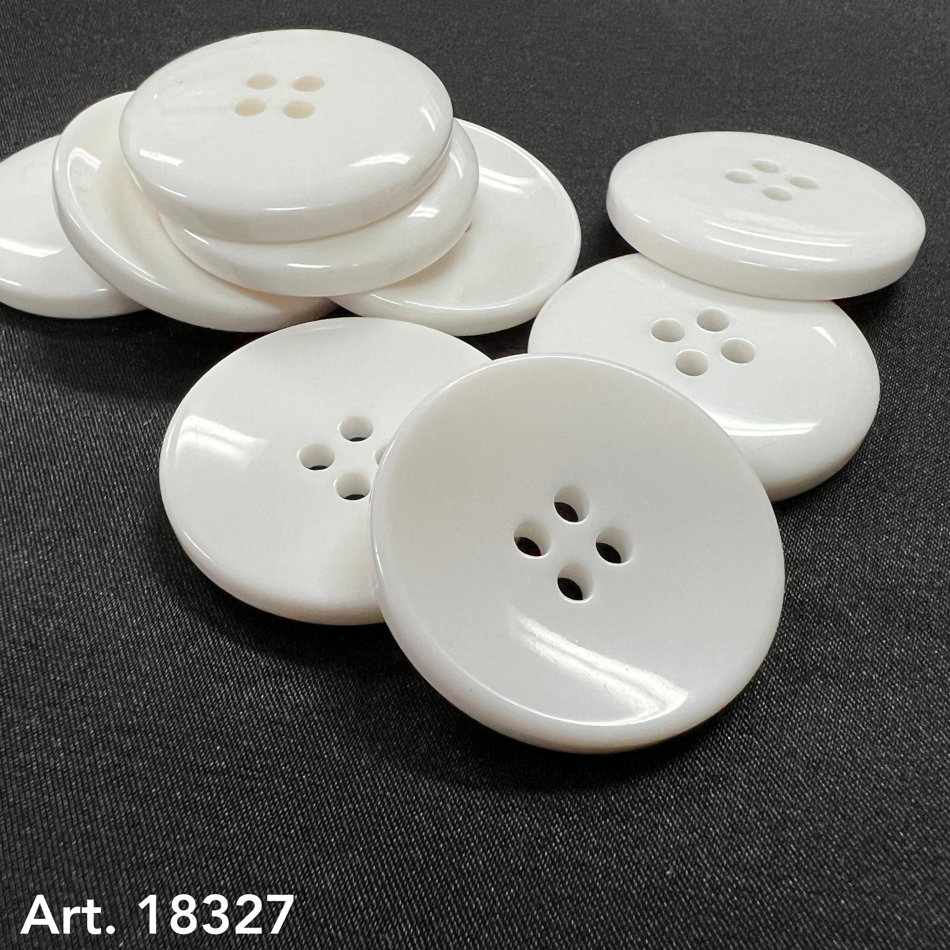 Close up of large white garment buttons by Buttonology Inc glossy four hole buttons on black fabric surface