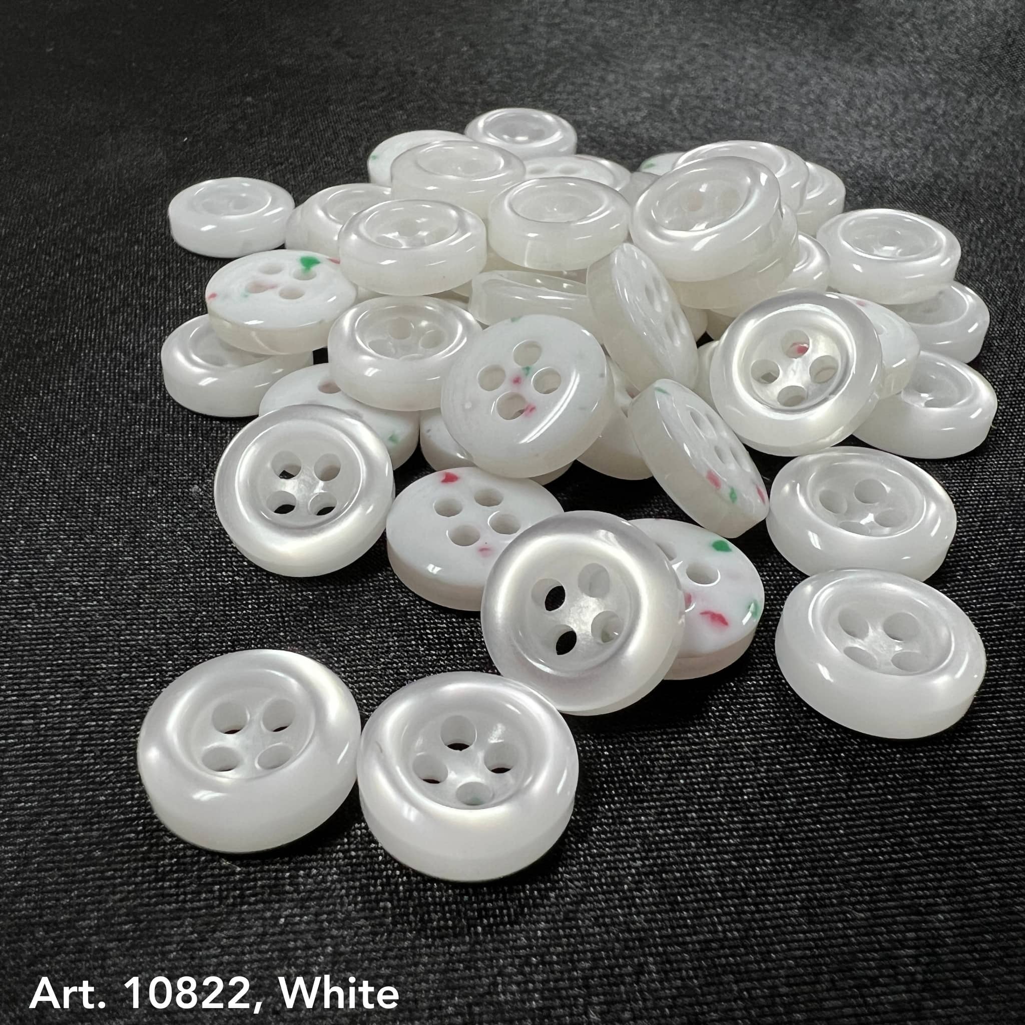 White sewing accessory buttons from Buttonology Inc with four holes on black fabric background