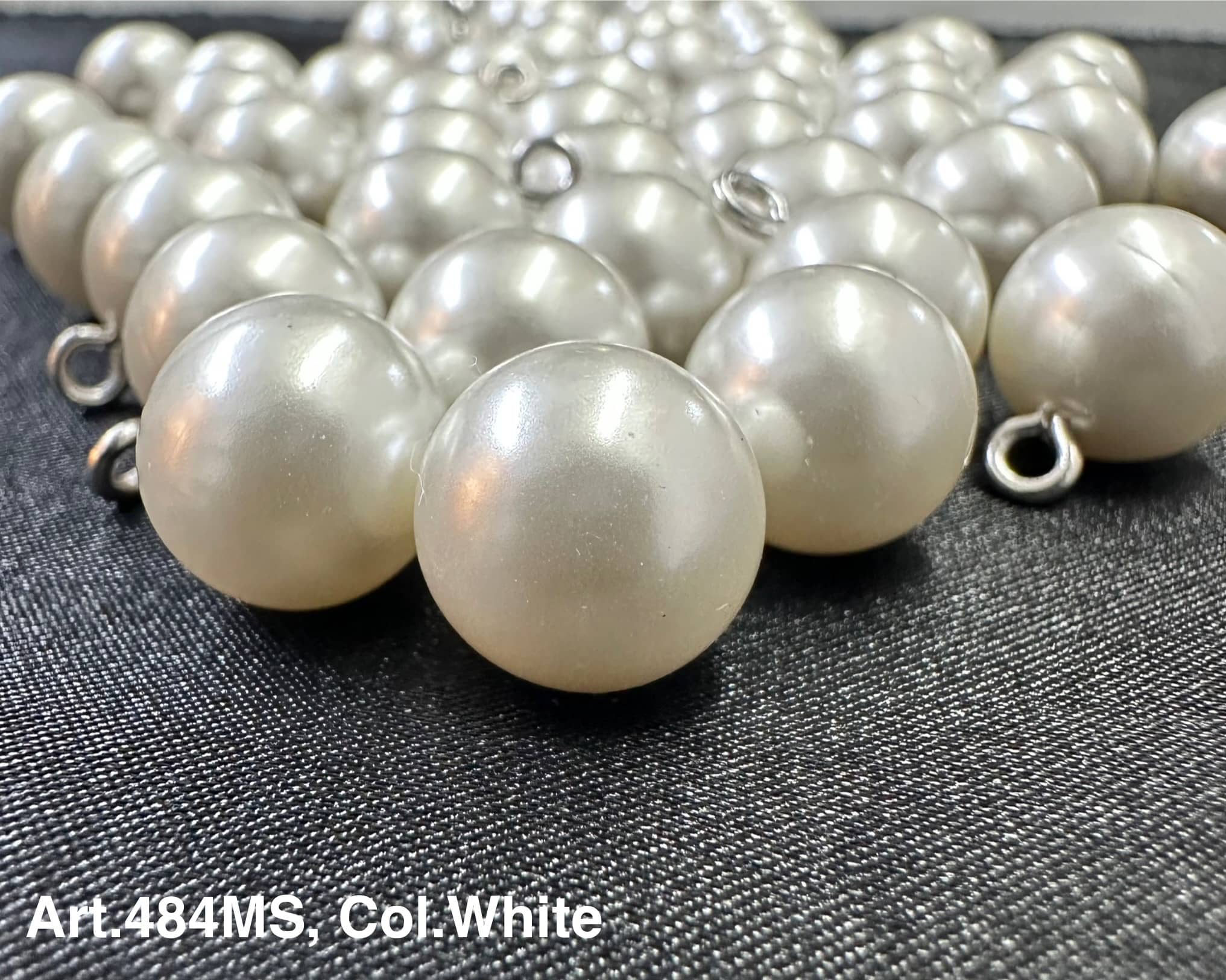 White pearl shank buttons for garments by Buttonology Inc displayed on black fabric