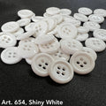 Shiny white sewing buttons from Buttonology Inc scattered on black fabric background