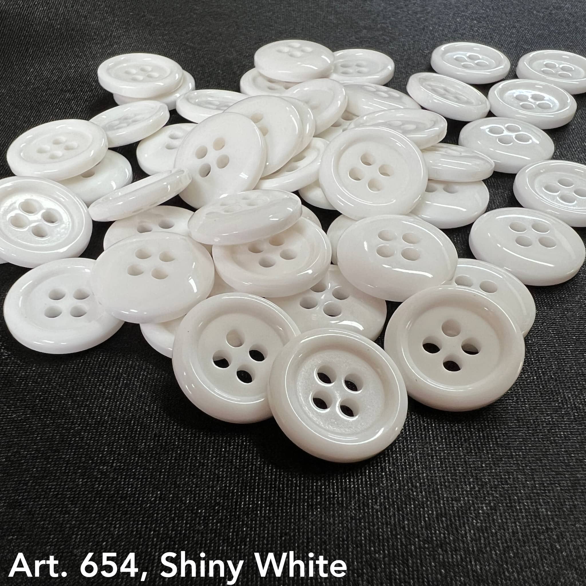 Shiny white sewing buttons from Buttonology Inc scattered on black fabric background