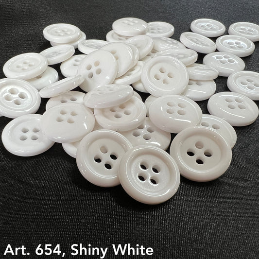 Shiny white sewing buttons from Buttonology Inc scattered on black fabric background