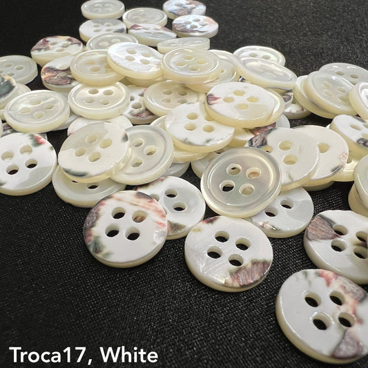 Troca shell buttons for garments in white with four holes by Buttonology Inc scattered on a black surface