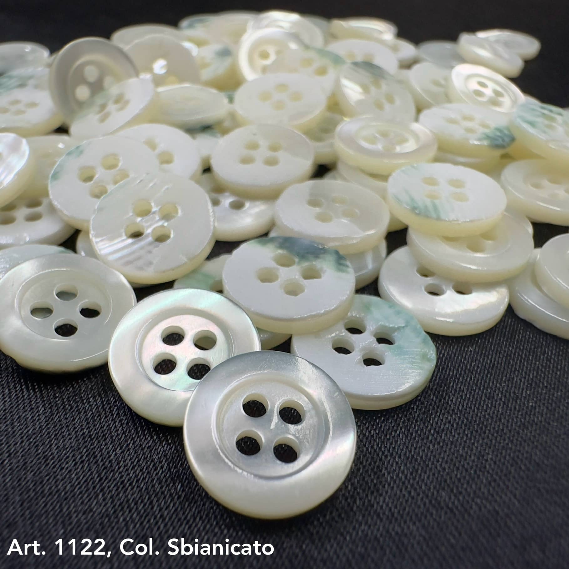 Troca shell buttons by Buttonology Inc with pearly white finish and four holes on black fabric background