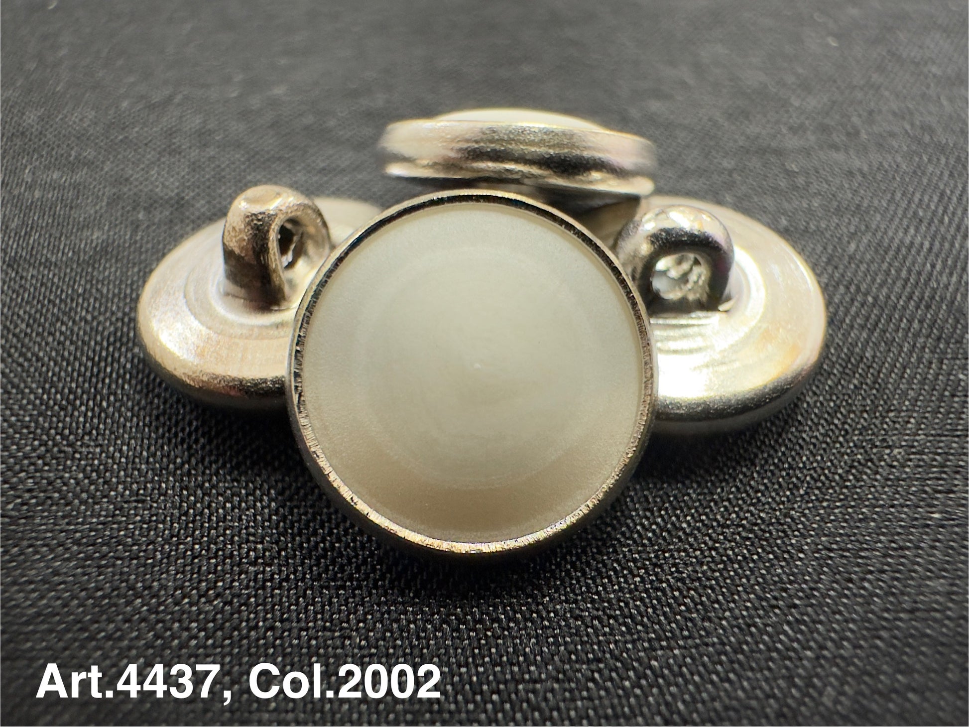 Buttonology Inc urea shank buttons in silver with round smooth surface on black fabric background