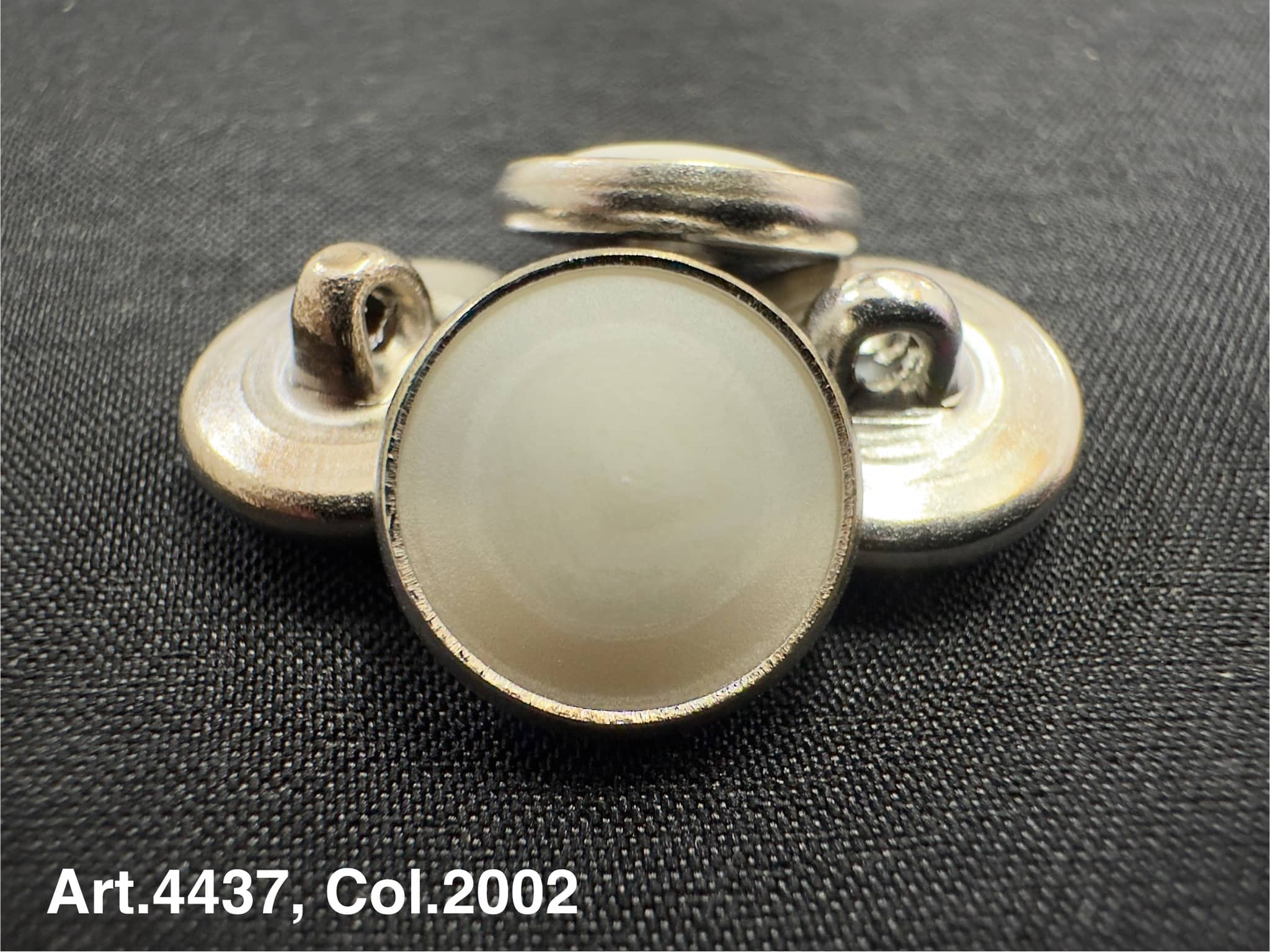 Buttonology Inc urea shank buttons in silver with round smooth surface on black fabric background