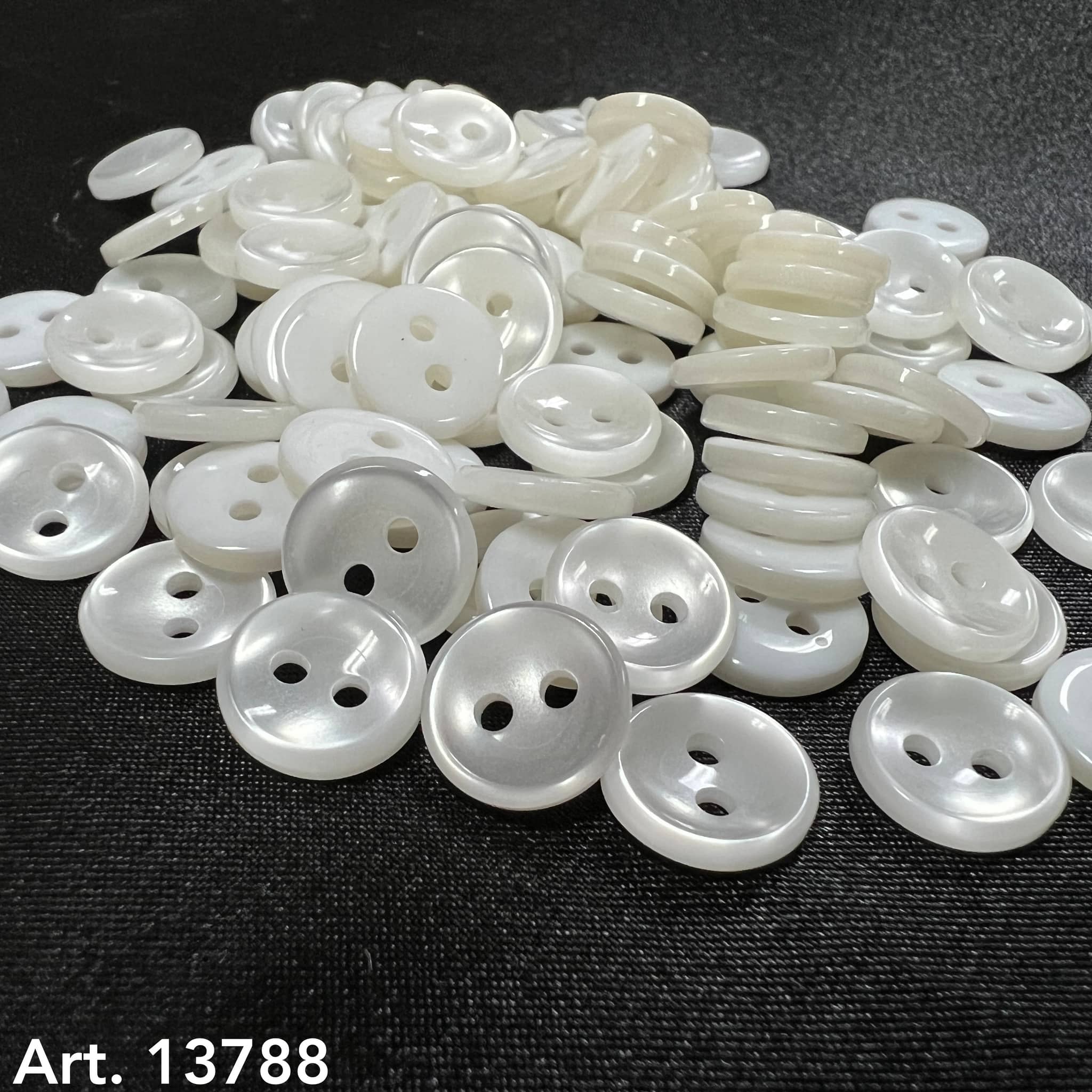 White 2 hole buttons by Buttonology Inc stacked on black fabric surface