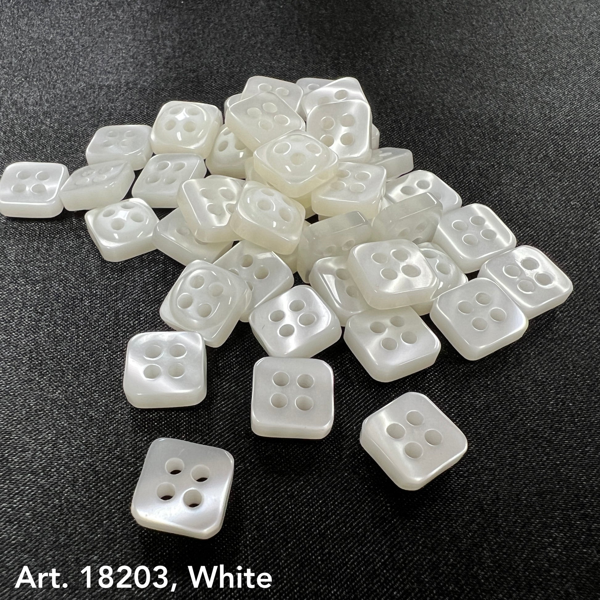 White square sewing buttons with four holes by Buttonology Inc. arranged on black fabric