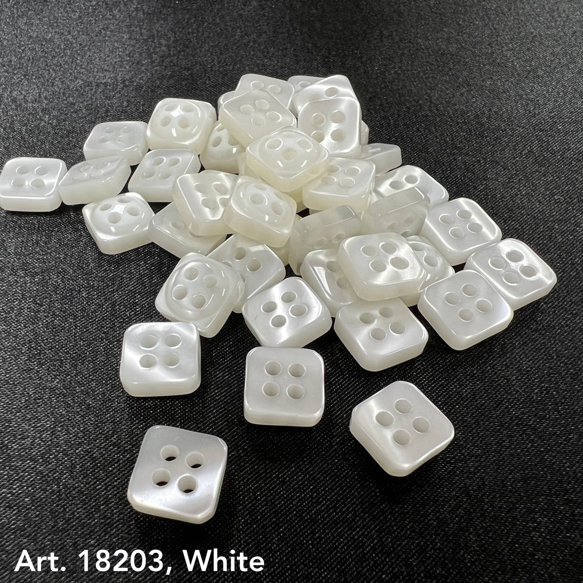 White square sewing buttons with four holes by Buttonology Inc. arranged on black fabric