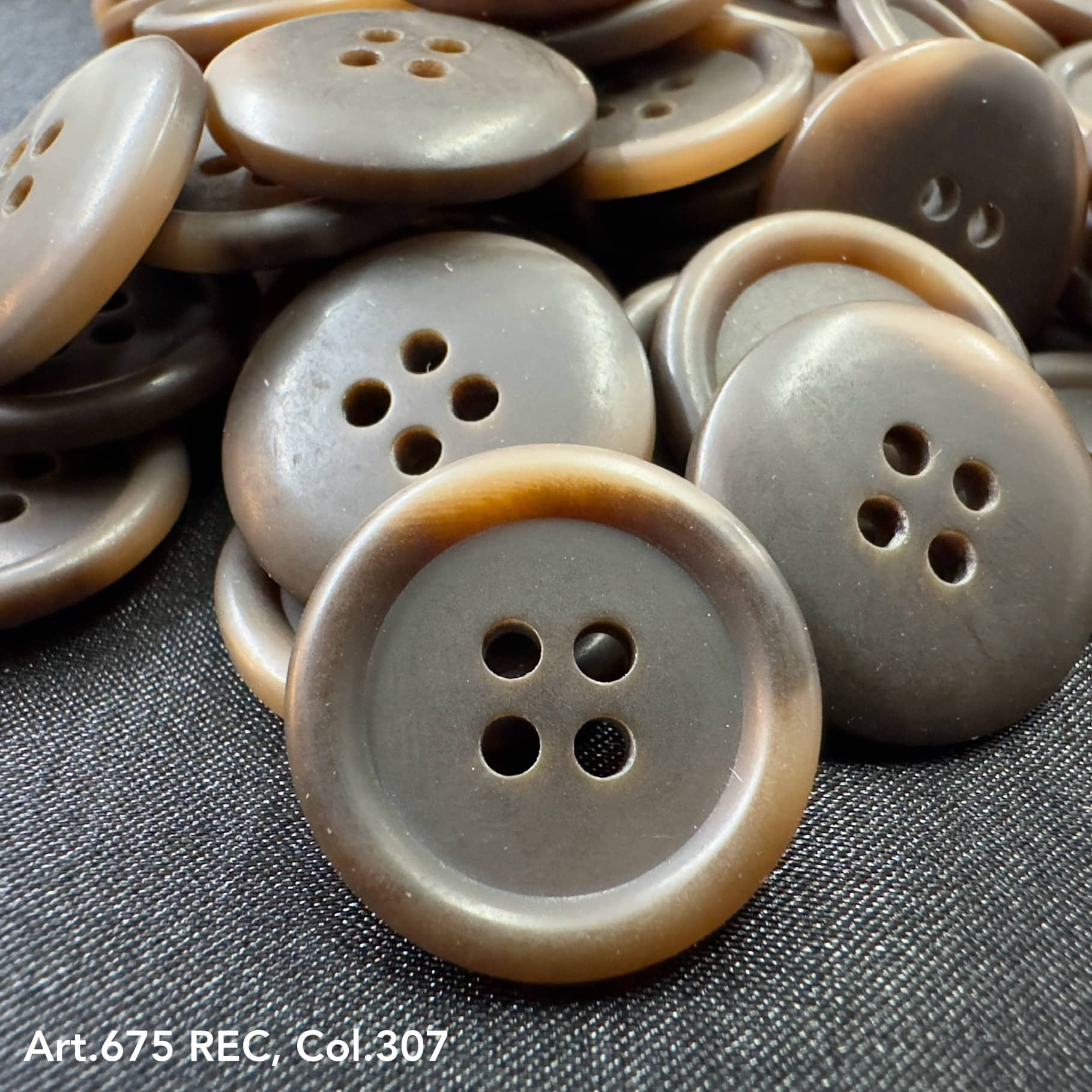 Wholesale four-hole buttons in brown shades by Buttonology Inc with a smooth finish stacked on fabric