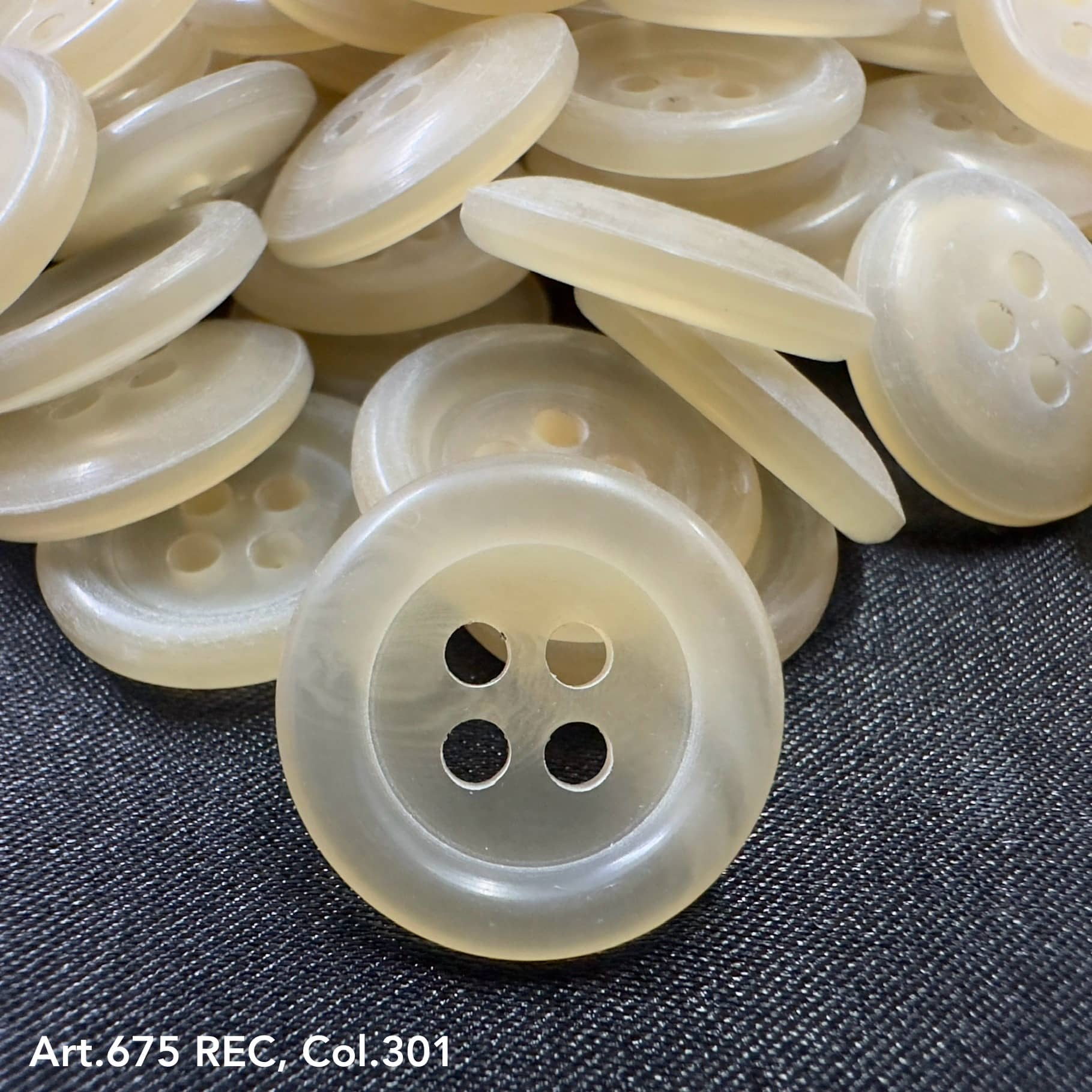 Wholesale four-hole buttons in translucent cream color by Buttonology Inc, stacked on dark fabric